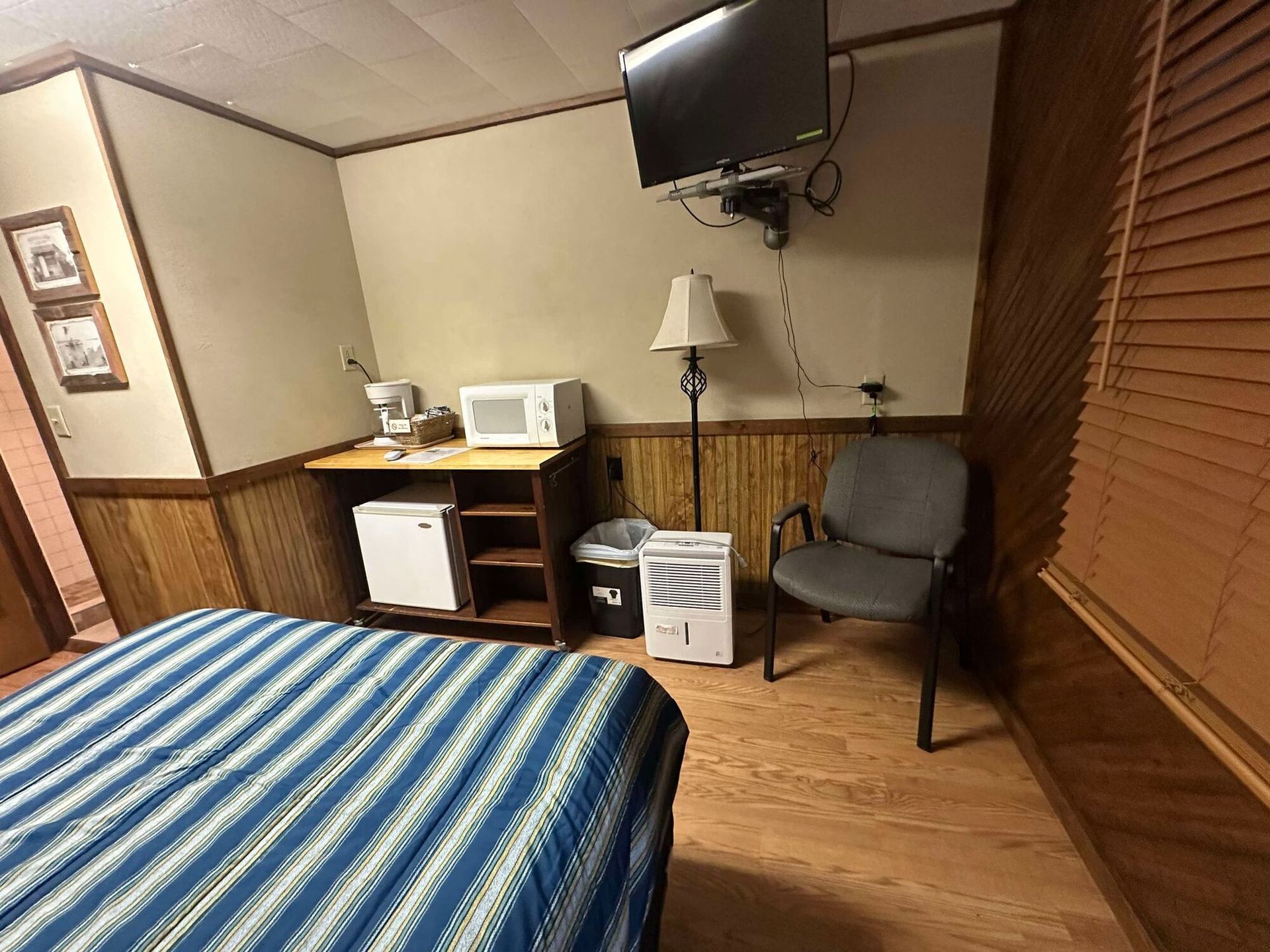 A hotel room with a bed , chair , microwave and television.