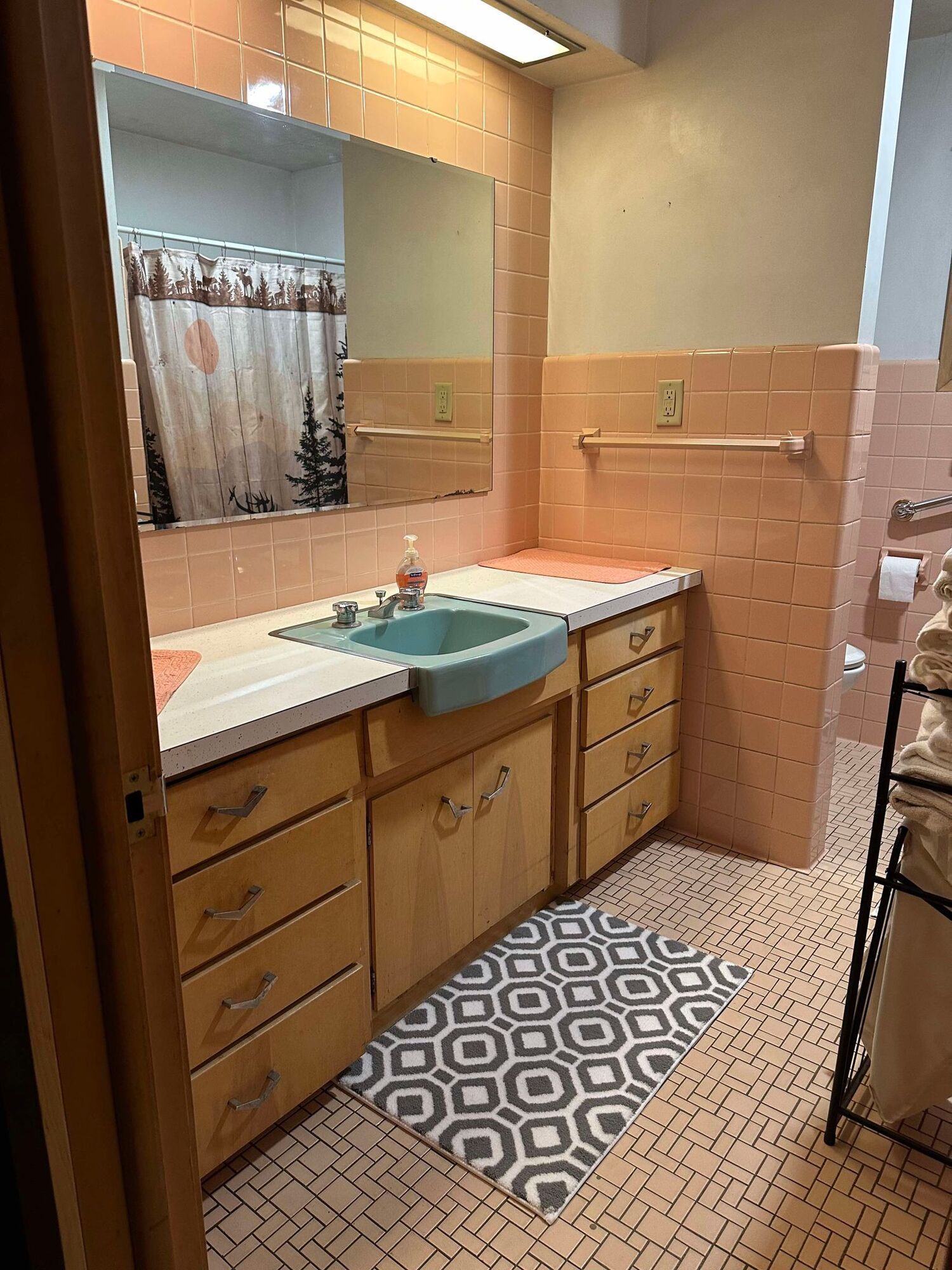 A bathroom with pink tiles , a sink , a mirror and a rug.