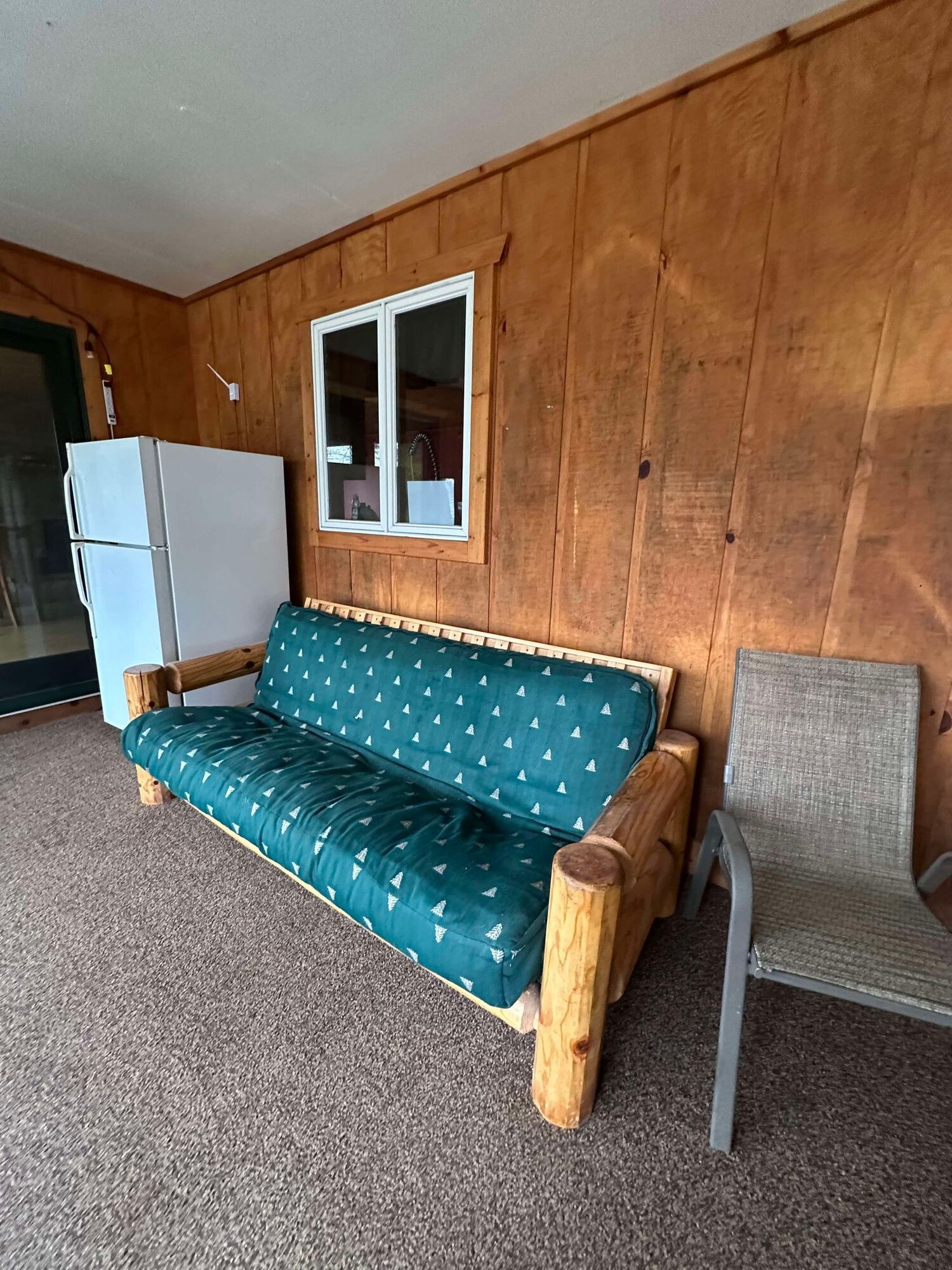 A couch is sitting on a porch next to a chair and a refrigerator.
