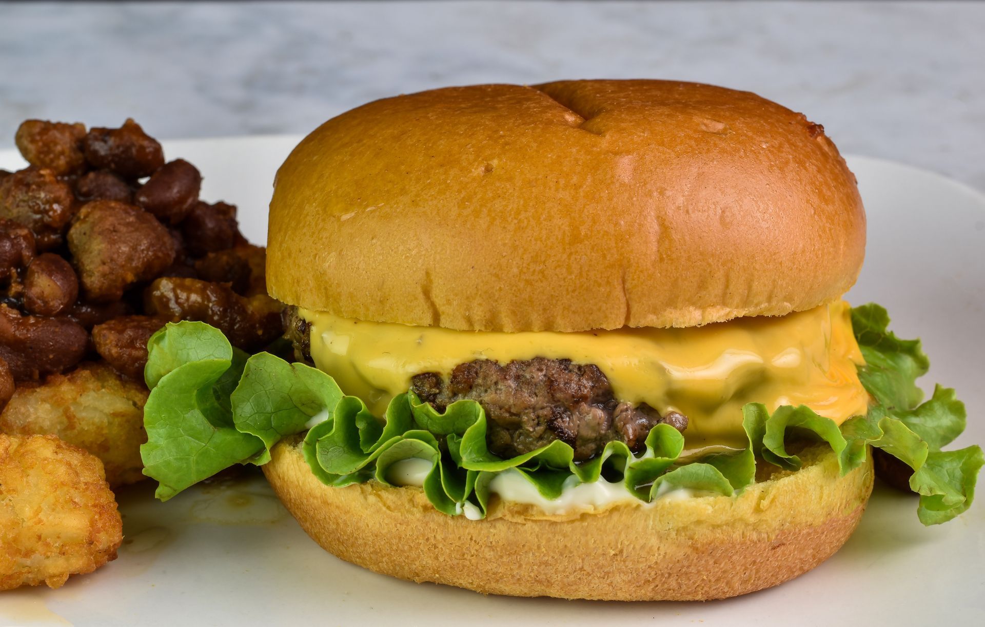 A close up of a hamburger on a plate with lettuce and beans.