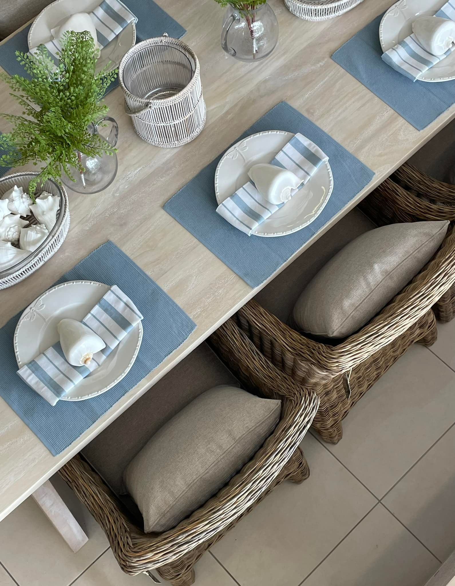 A Dining Table Set with Blue Placemats, White Plates, and Woven Chairs with Beige Pillows — Tropic Living in Kewarra Beach, QLD