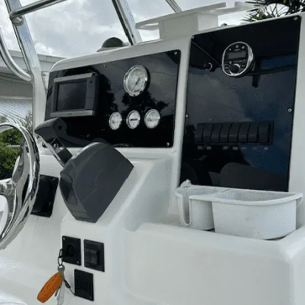 Boat dashboard with gauges, switches, and steering wheel, mostly white and black.
