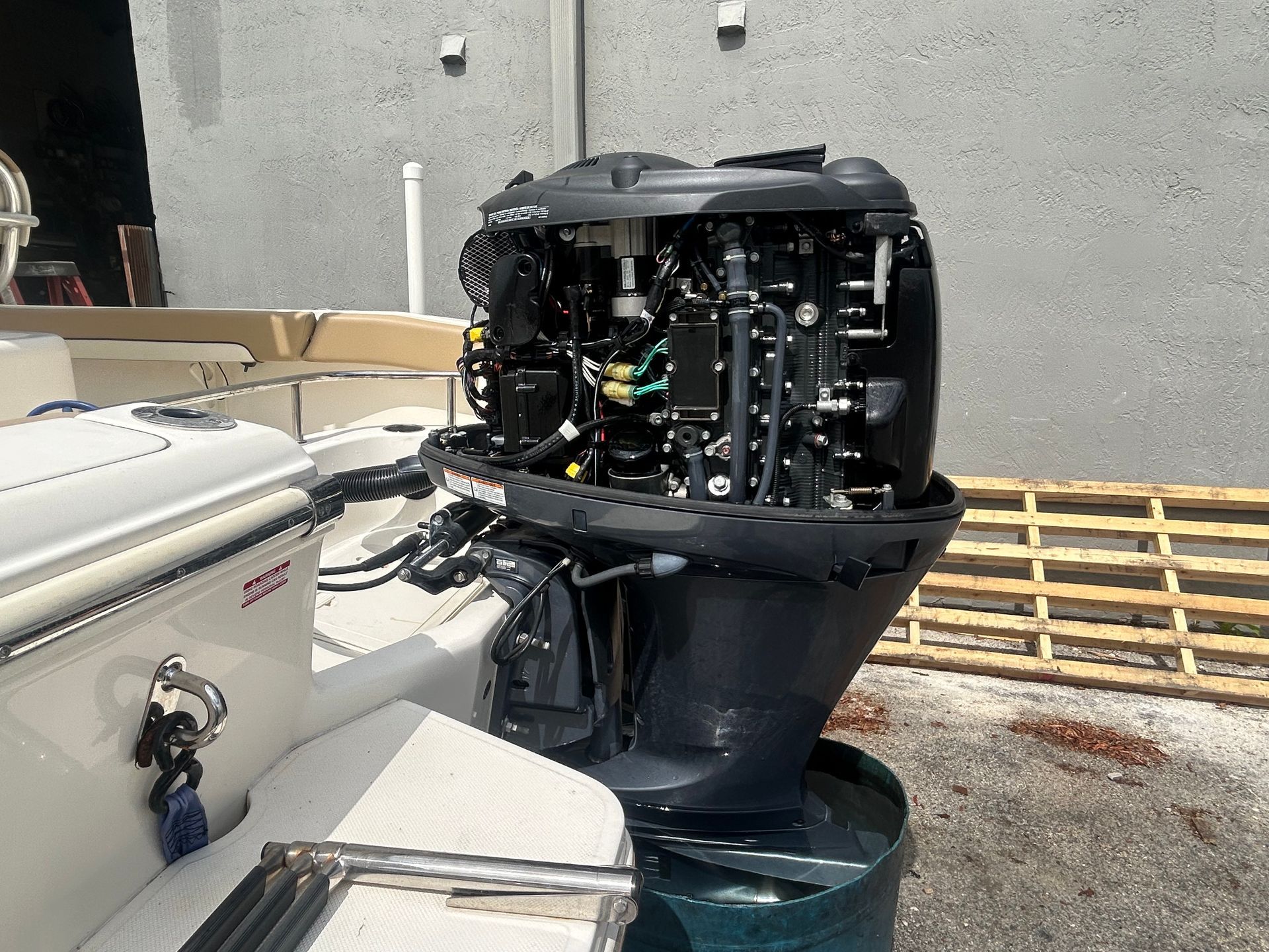 Outboard motor mounted on a boat, black and gray against a light wall and wooden pallet.