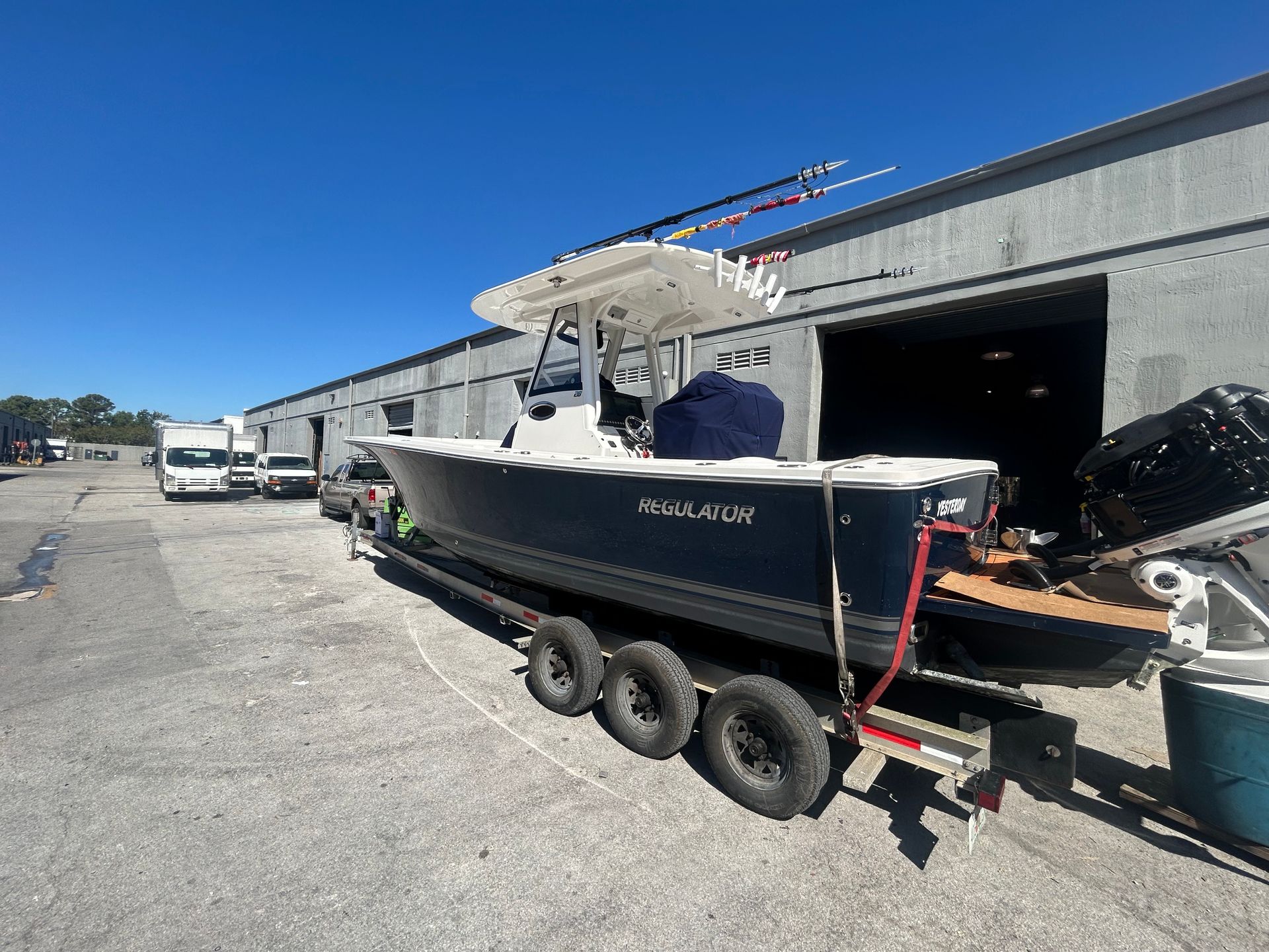 A blue and white motorboat on a trailer in front of a warehouse on a sunny day.