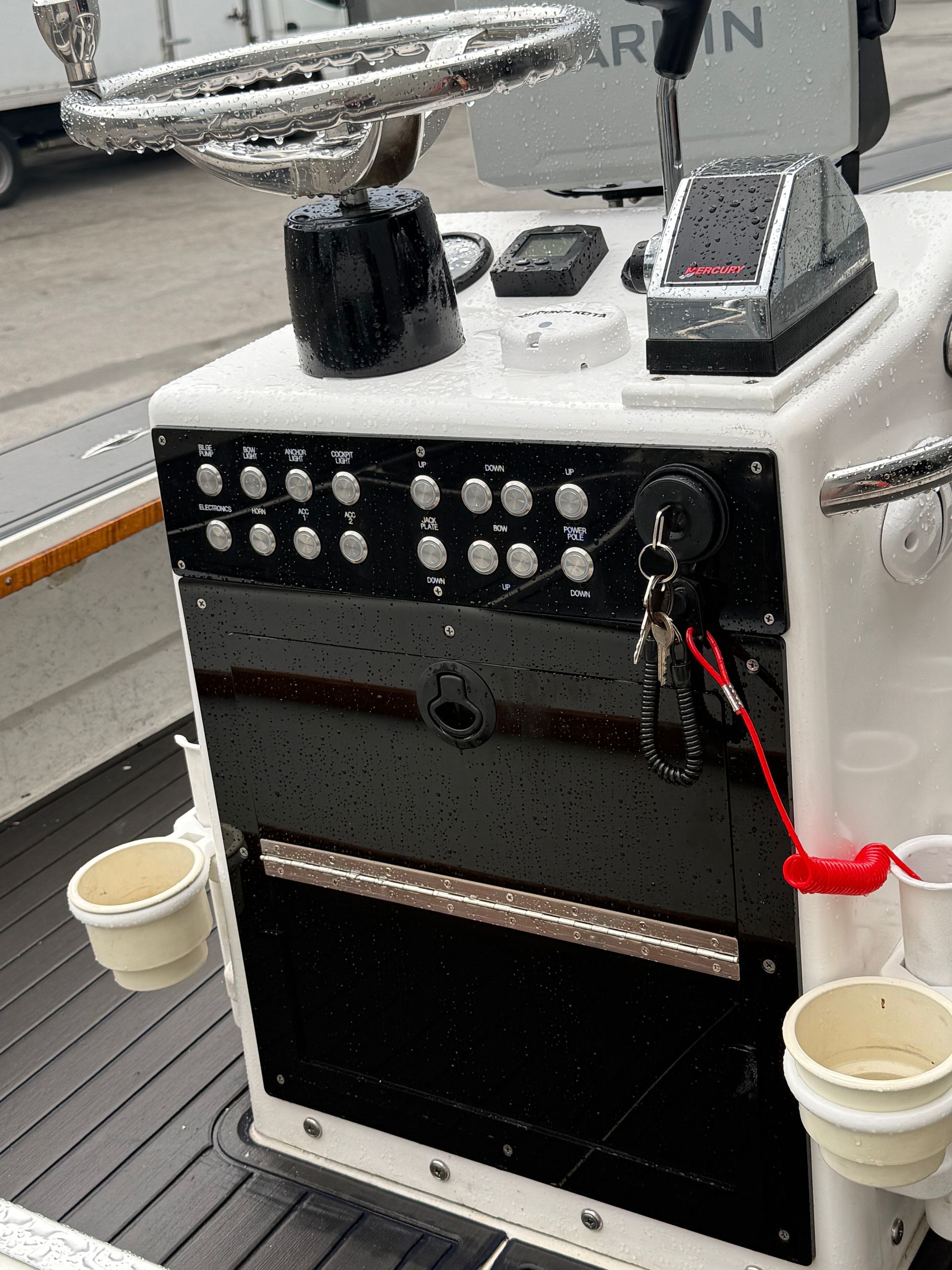 Boat helm with steering wheel, gauges, switches, and cup holders.