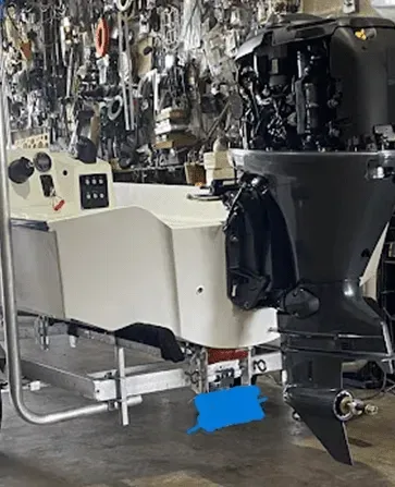 White boat on trailer, black motor attached. Workshop background with tools.