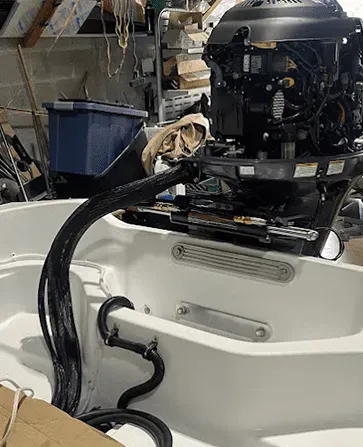 A boat motor installed in a white boat, with black tubing and wires. Garage setting.