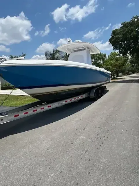 Blue and white boat on a trailer, parked on asphalt under a blue sky with clouds.