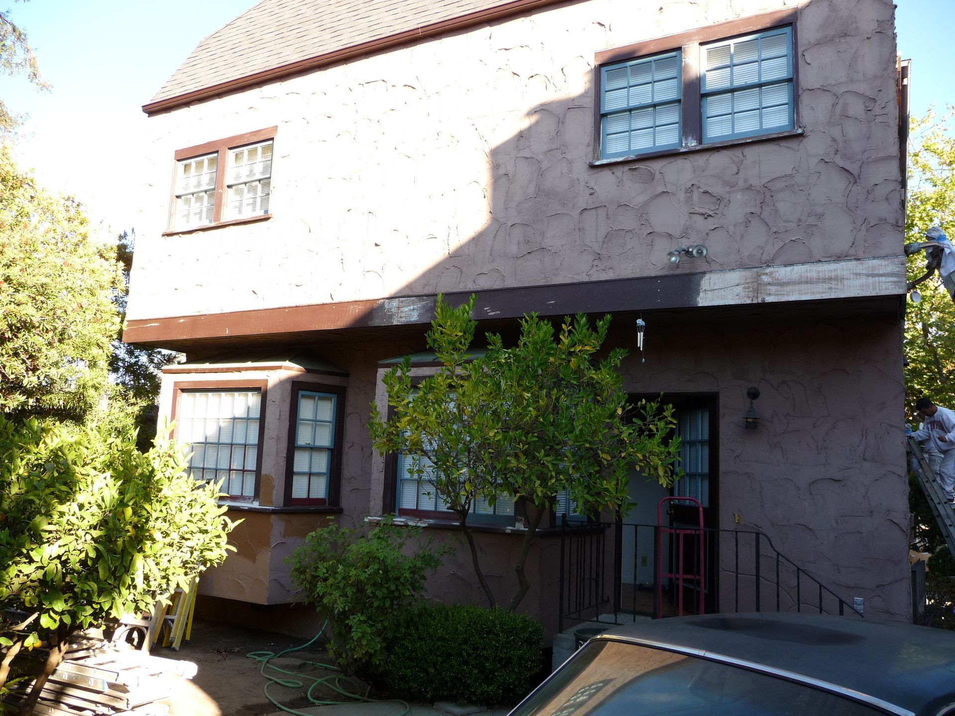 Two-story stucco house with brown trim and windows. A small tree grows in front.