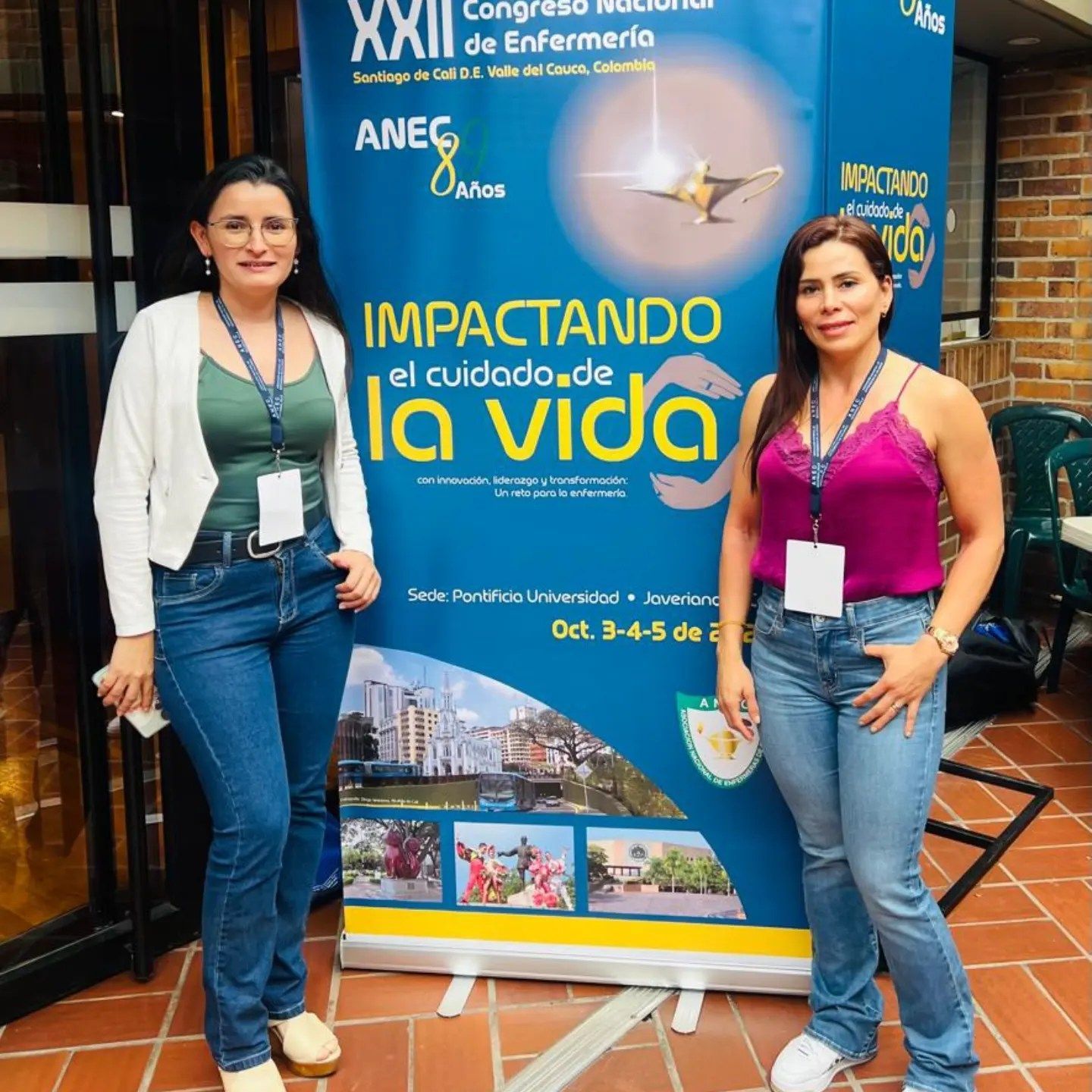 Dos mujeres están de pie frente a una pancarta de la conferencia. La pancarta dice