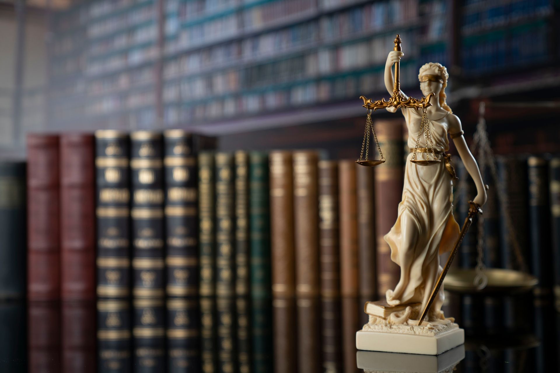 A statue of justice is sitting on a table in front of a bookshelf.