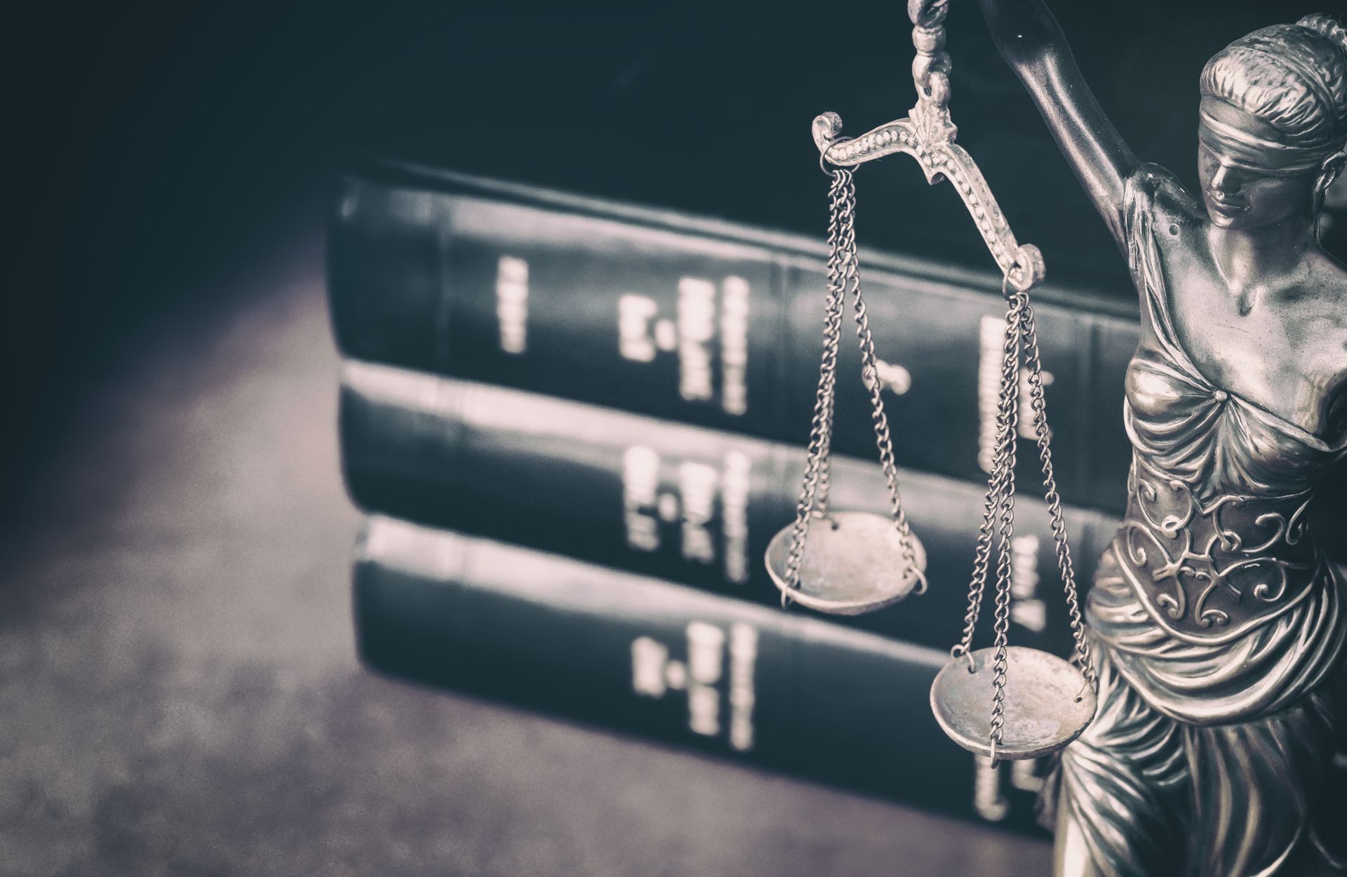 A statue of lady justice holding a scale in front of a stack of books.