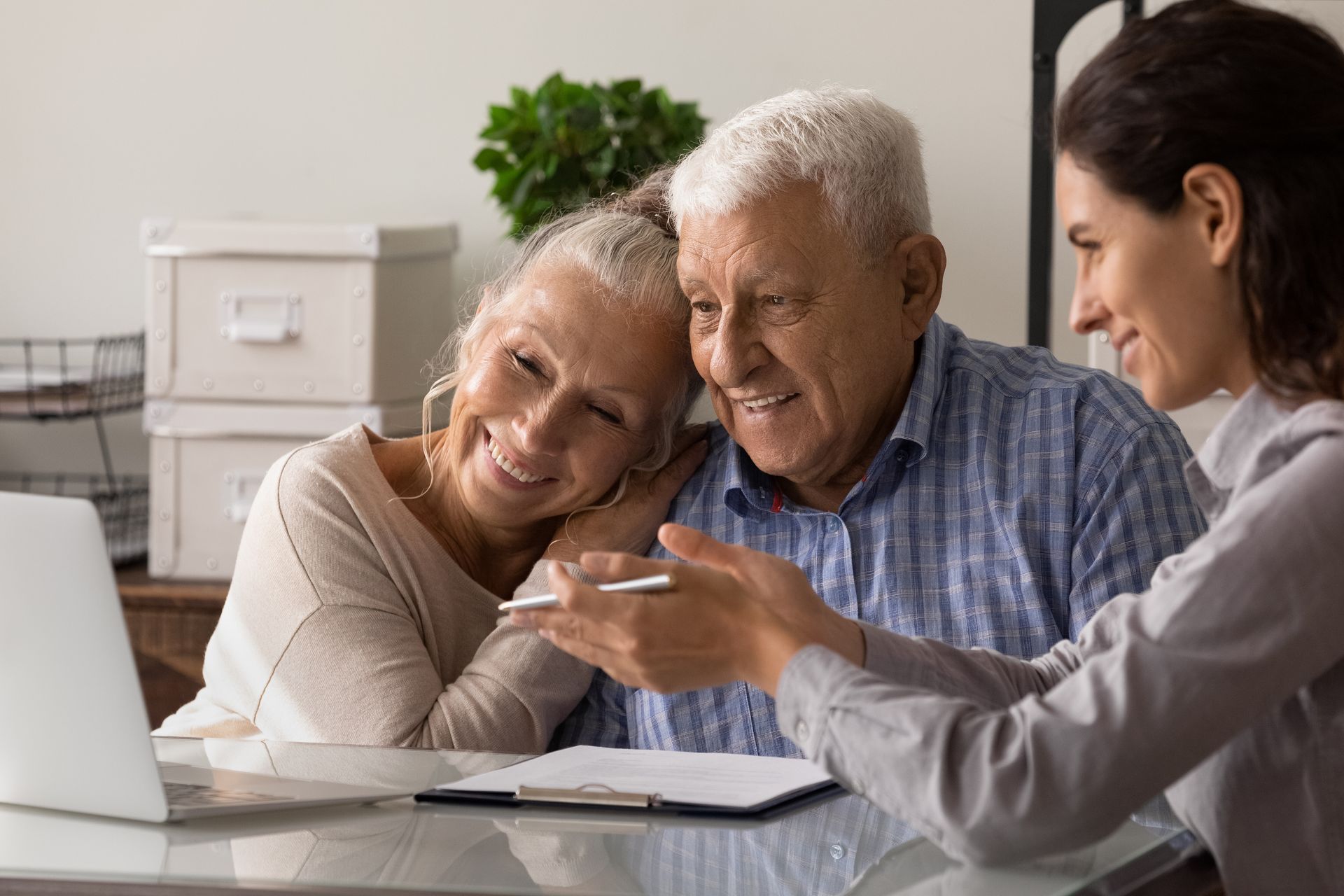 An elderly couple is sitting at a table with a woman looking at a laptop.