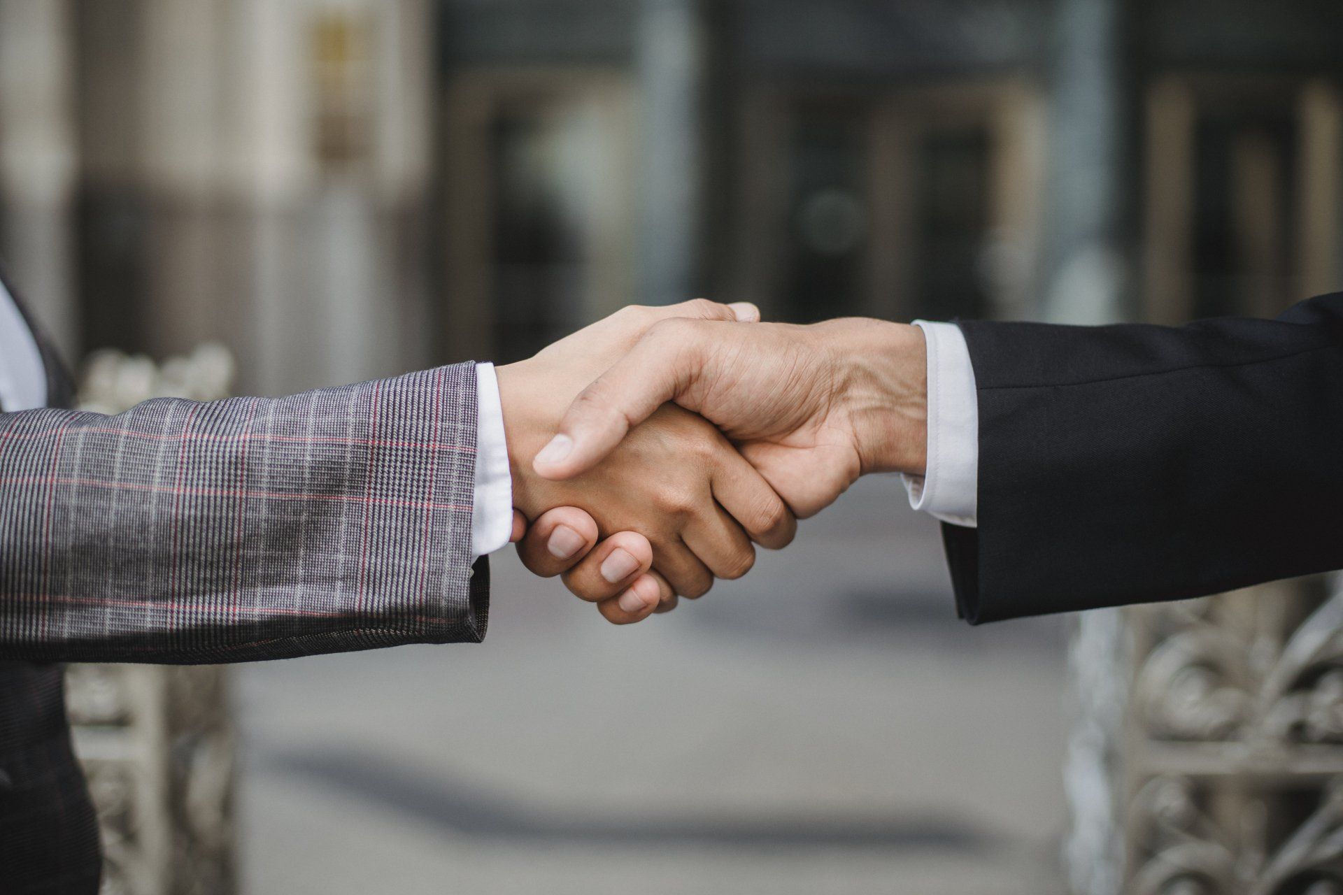 Two men are shaking hands in front of a building.