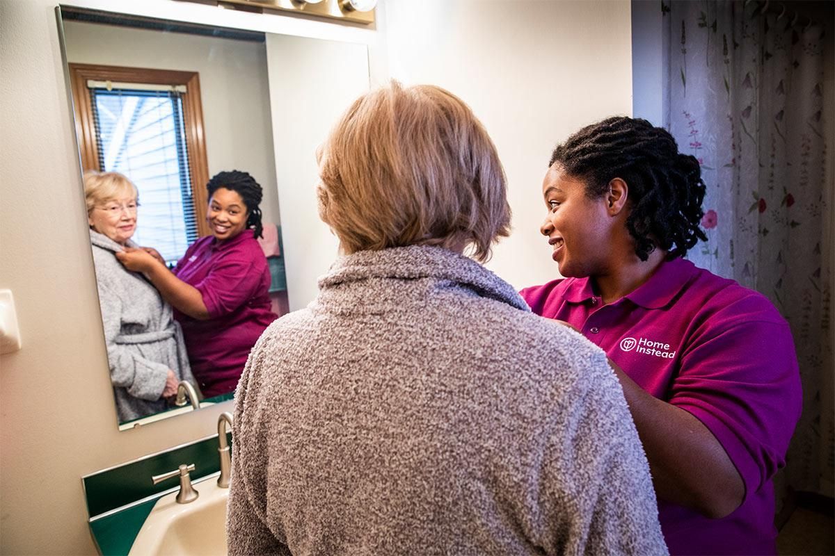 a woman is helping an older woman dress in front of a mirror .