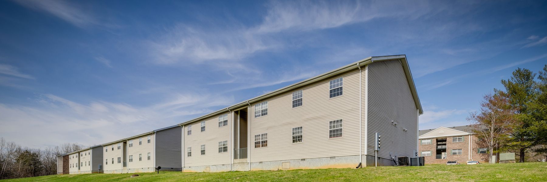 A large apartment building is sitting on top of a grassy hill.