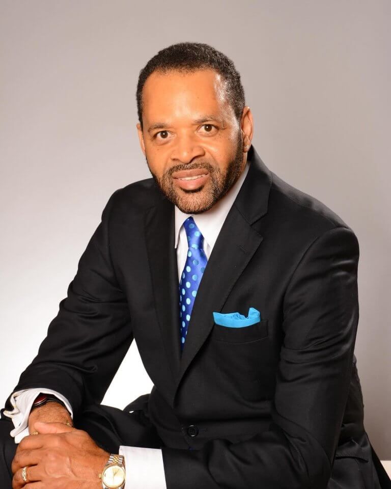 Man in a suit smiles, blue polka-dot tie, aqua pocket square. Studio setting, seated. Man in a suit smiles, blue polka-dot tie, aqua pocket square. Studio setting, seated.