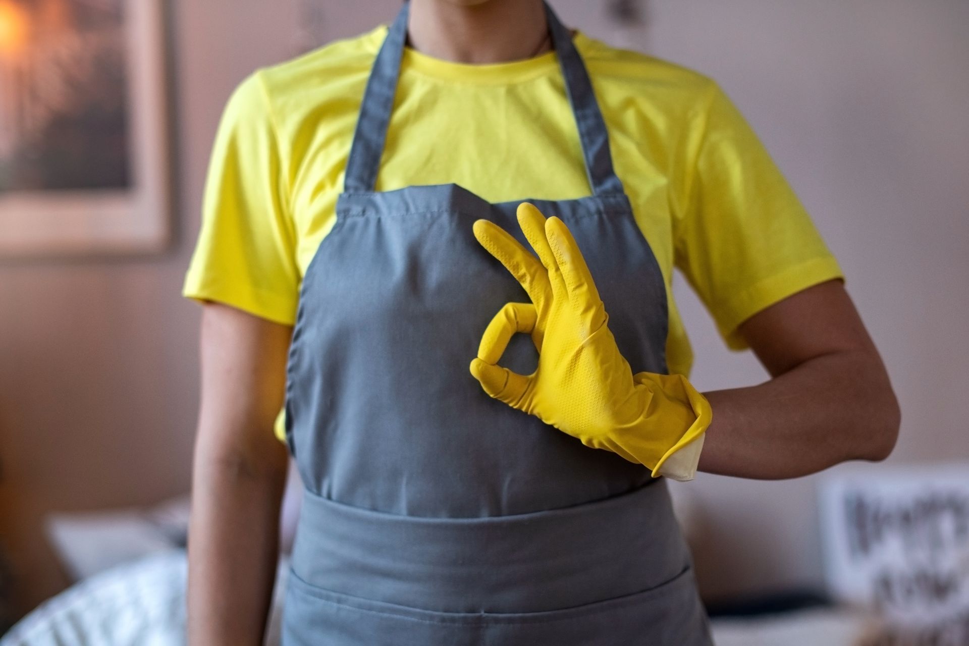 A woman wearing an apron and yellow gloves is giving an ok sign.