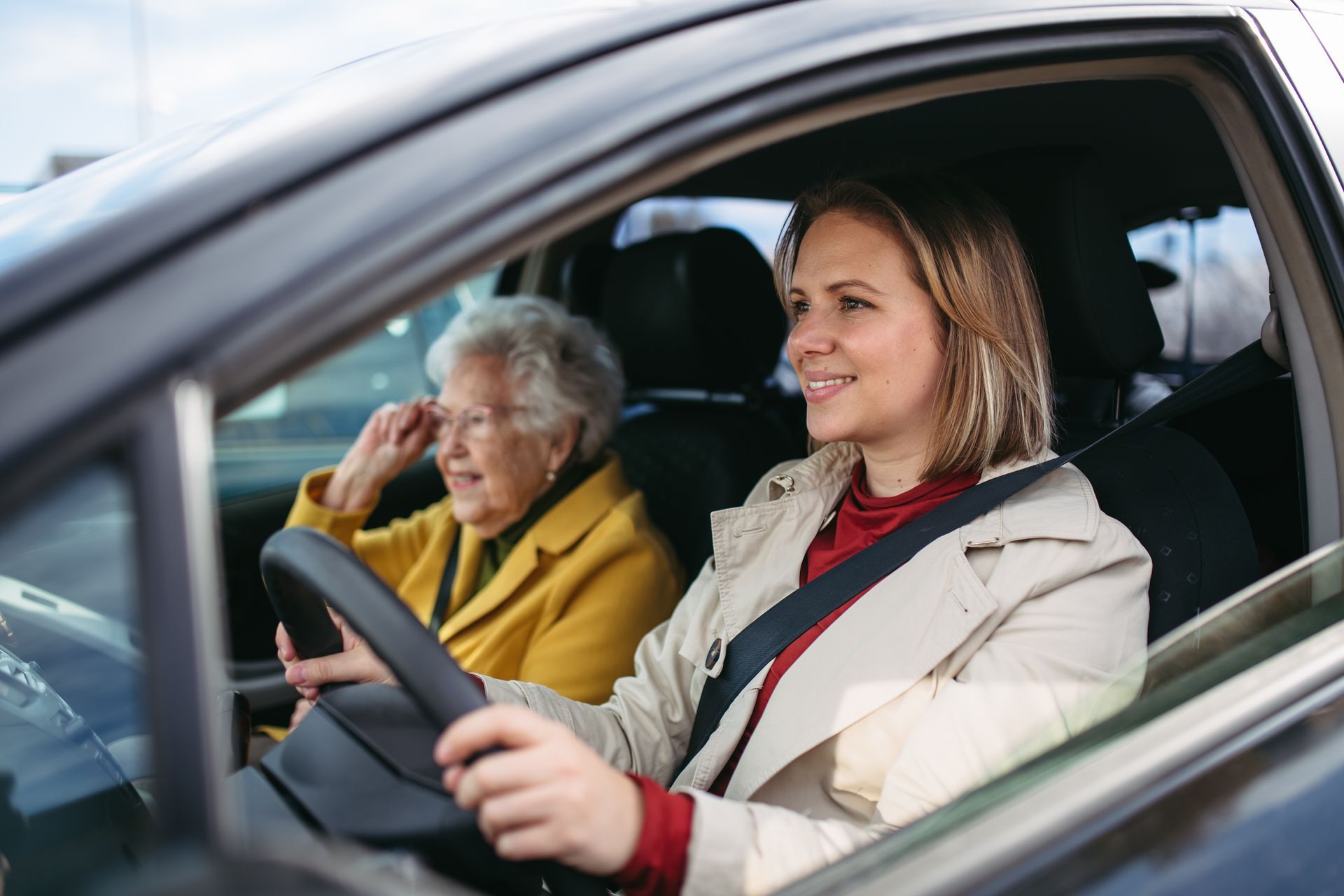 A woman is driving a car next to an older woman.