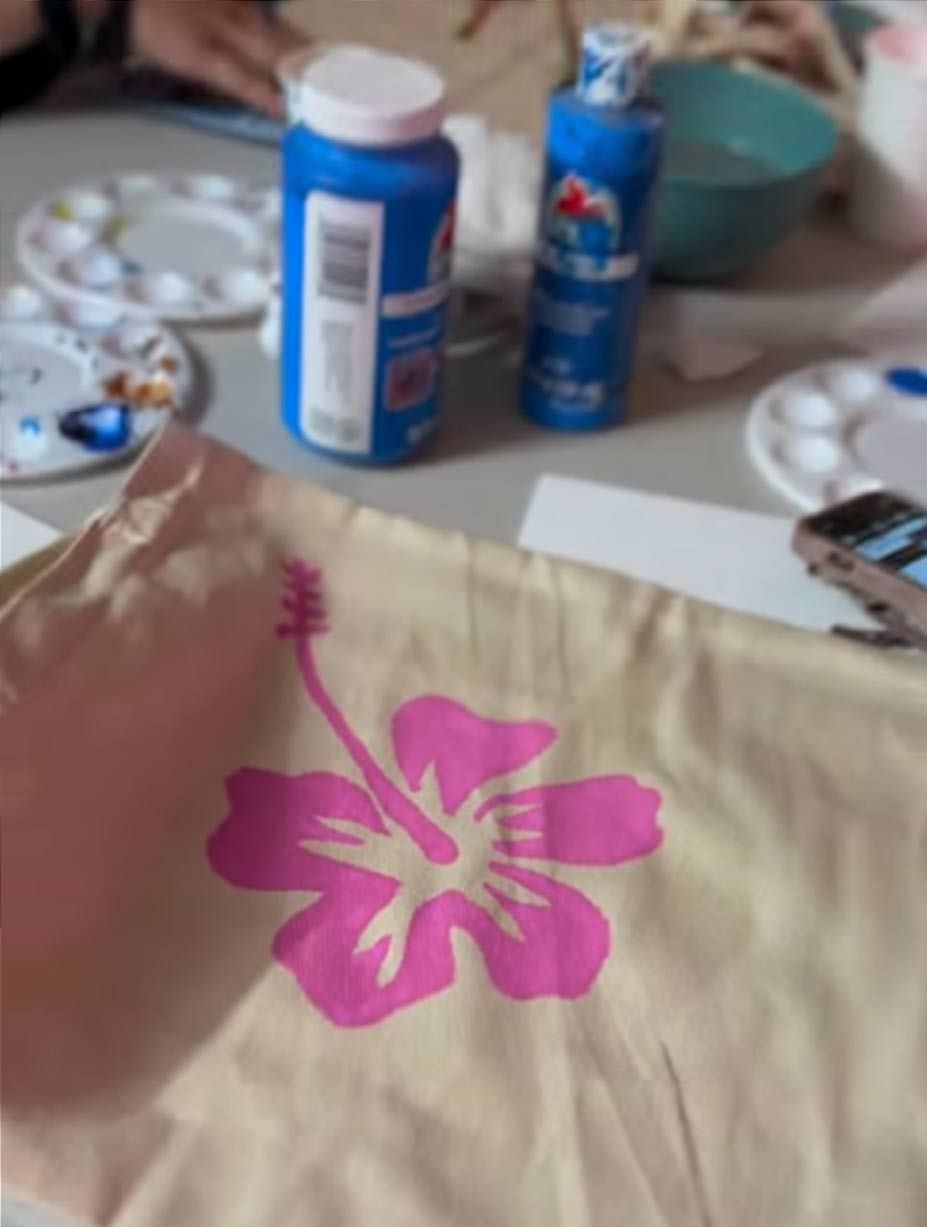 A person is painting a bag with a pink flower on it