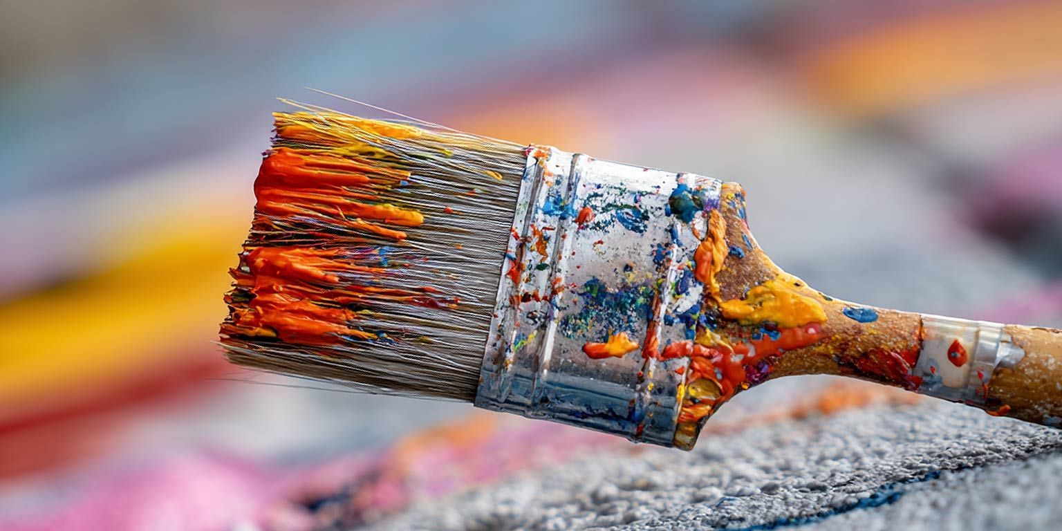 Close-up of a paint-covered paintbrush, with visible strokes of orange, yellow