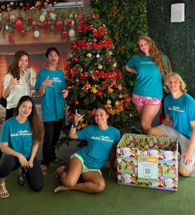Hands holding a box of food items, likely a donation. Crowd of people in the background.