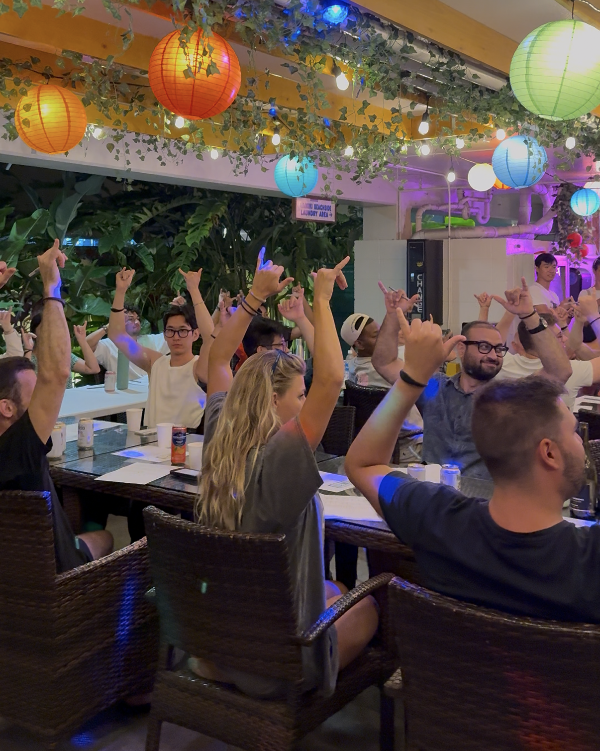 A group of people are sitting at tables with their arms in the air.