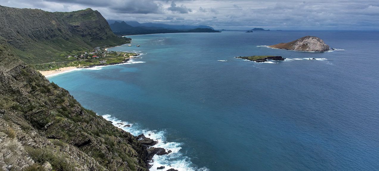 Scenic view of a coastline with a sandy beach, lush mountains, and islands in the ocean.