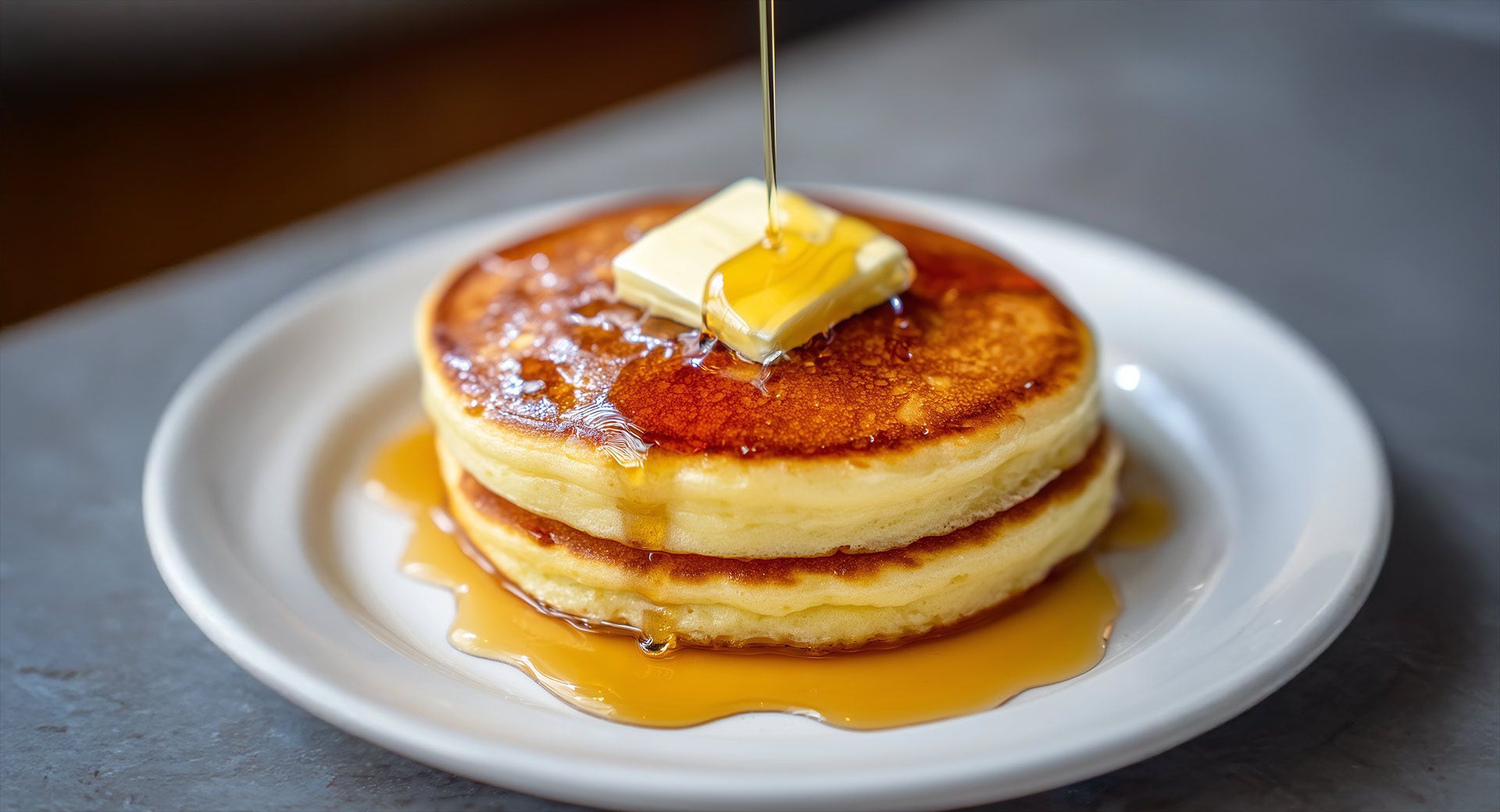 Stack of fluffy pancakes with melting butter and syrup.