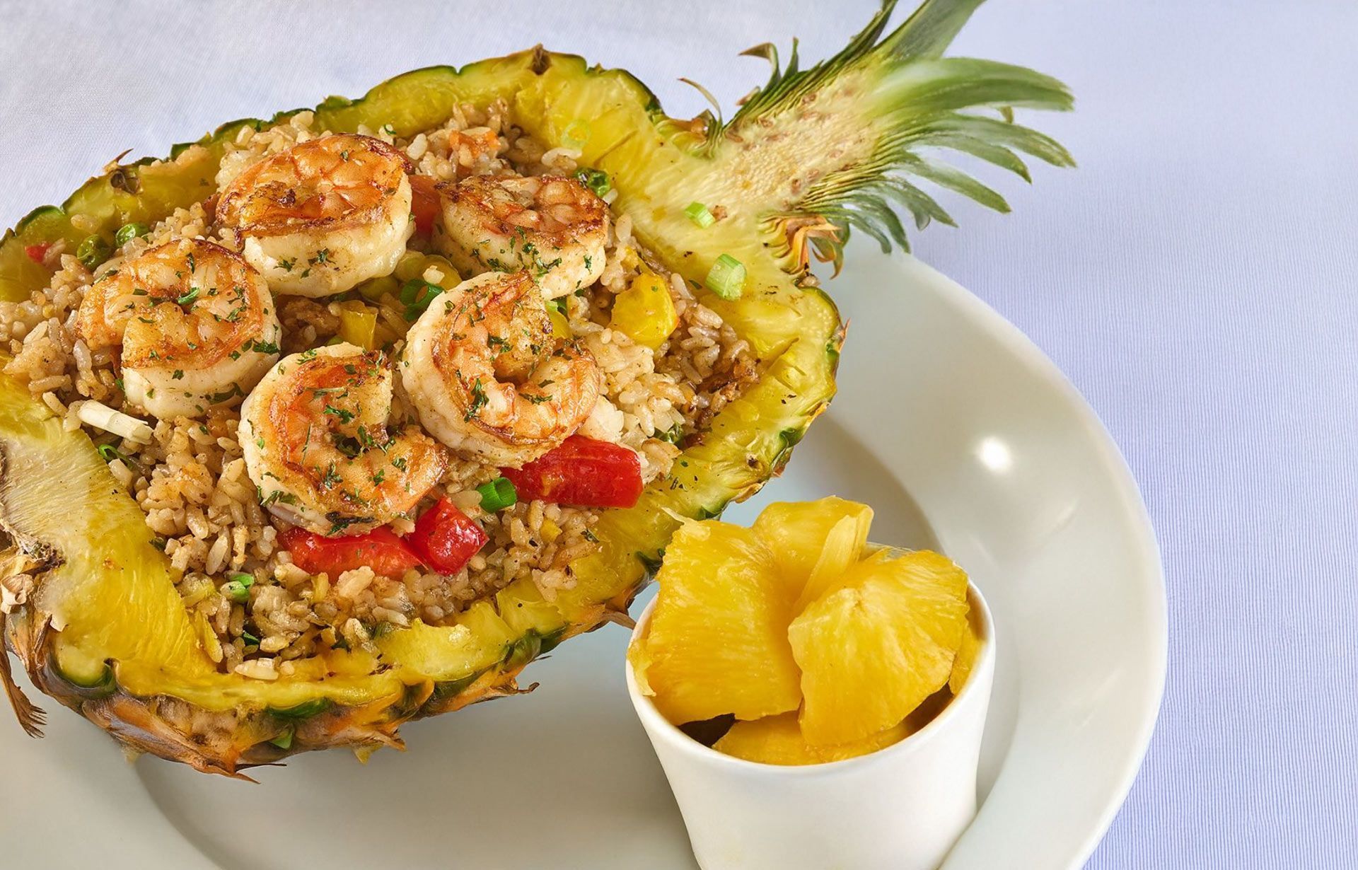 A pineapple filled with shrimp and rice next to a bowl of pineapple slices.