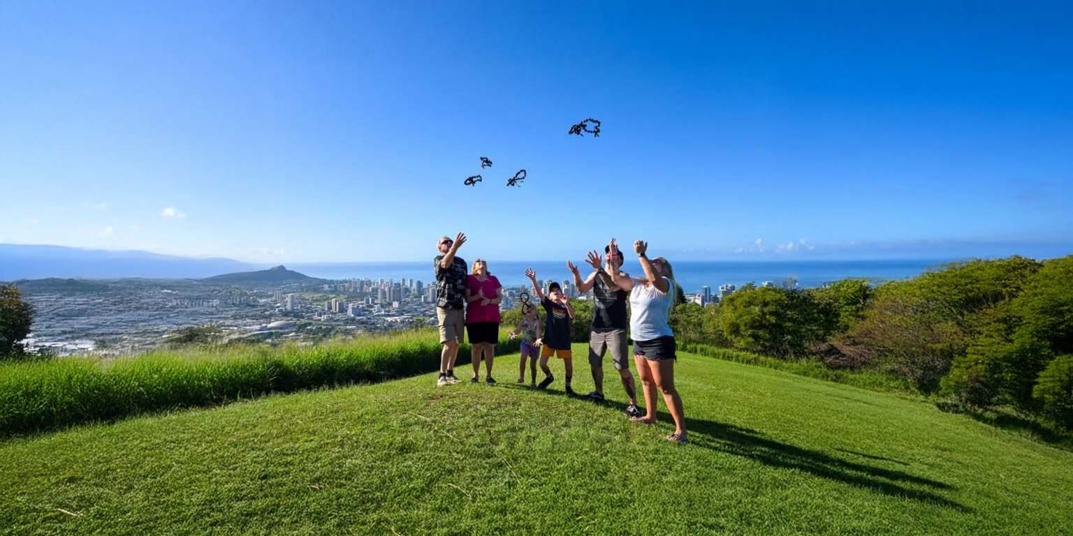 Group of people cheering, watching birds fly against a blue sky. City and ocean in background.