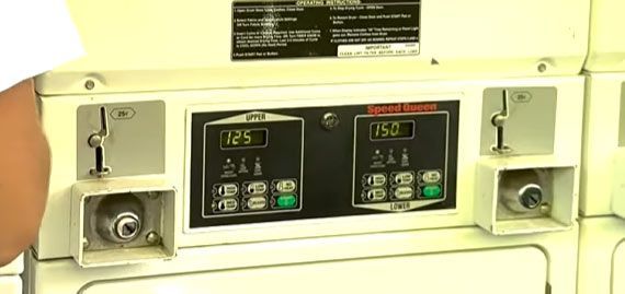 Close-up of a washing machine control panel showing digital displays with time and price, coin slots and buttons.