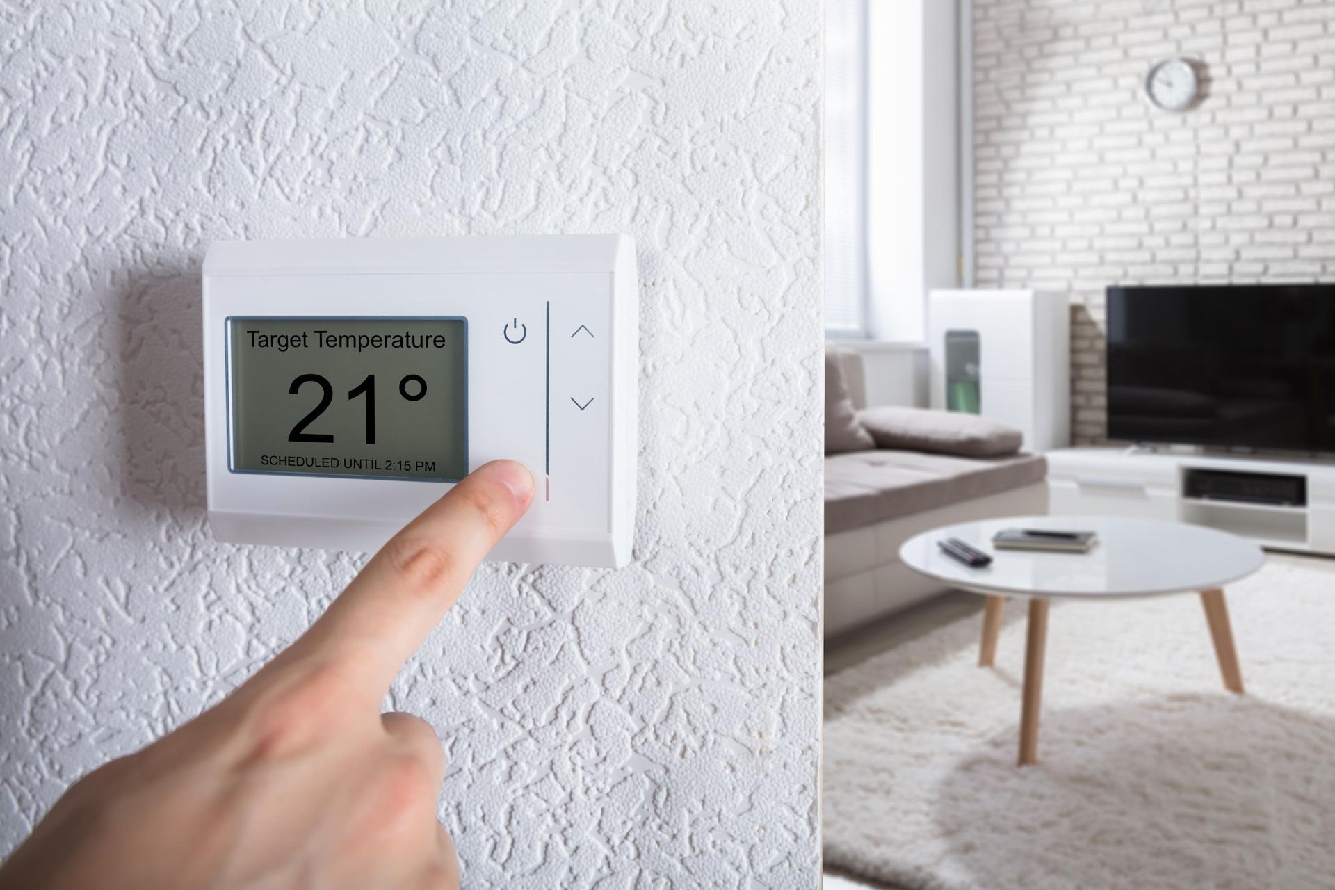 Person adjusting thermostat to 21 degrees in a living room with white walls and furniture.