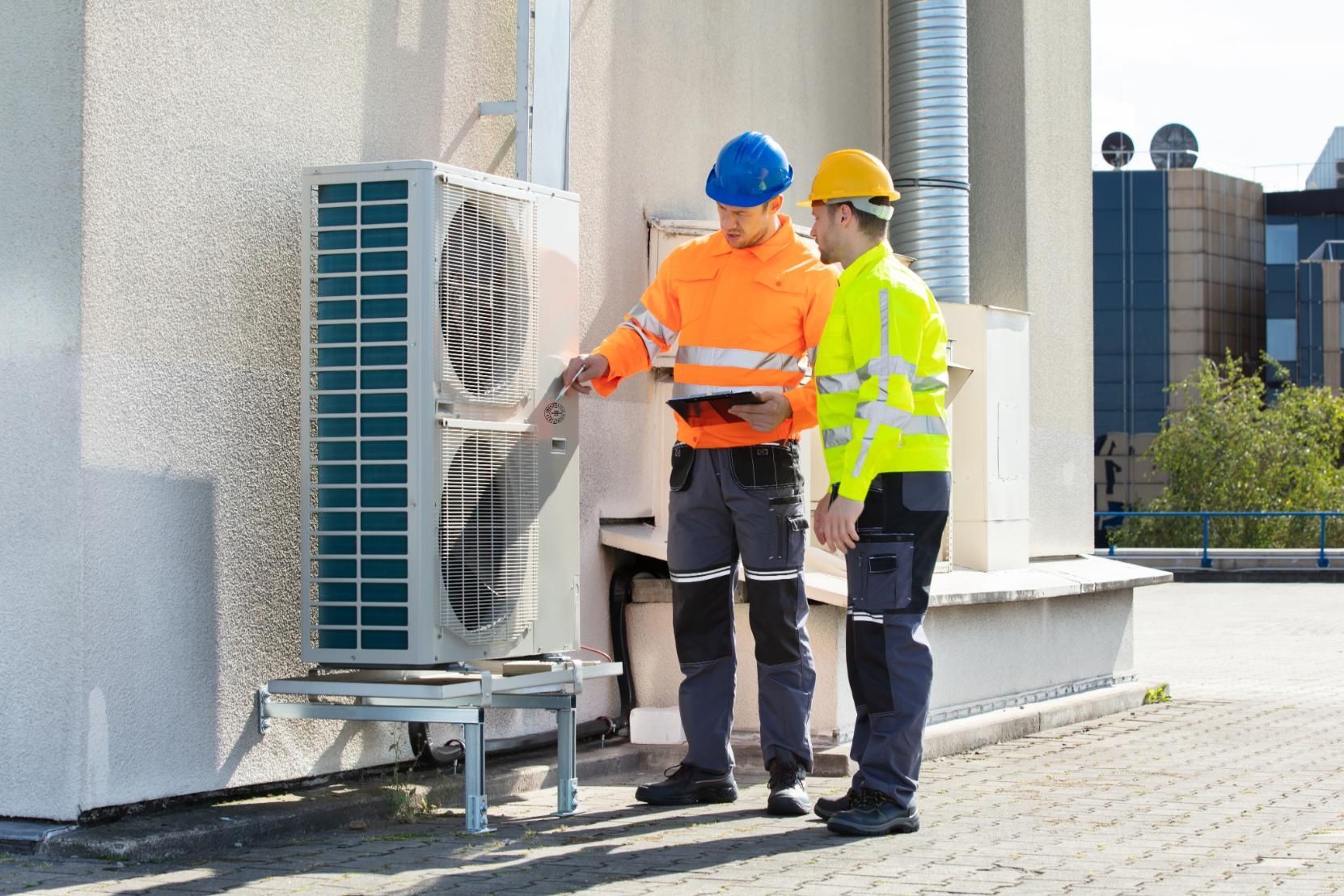 Two HVAC technicians examine an air conditioning unit on a rooftop.