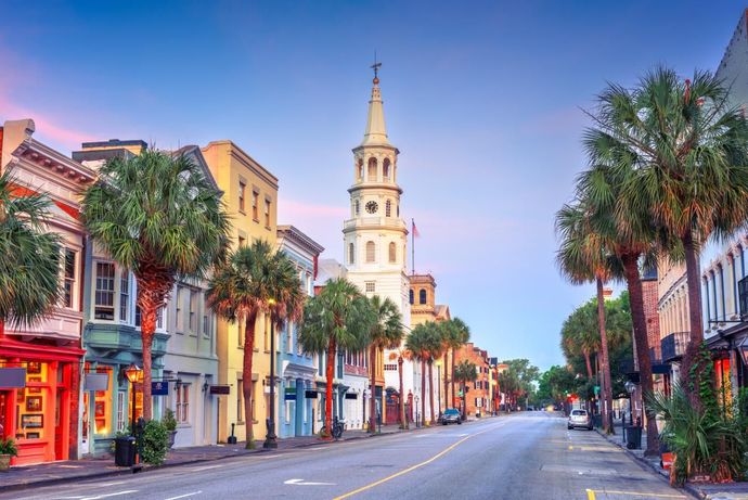 Colorful street in Charleston, SC, with palm trees lining the road, leading to a church steeple.