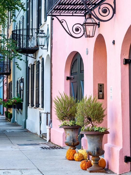 Colorful row houses with arched doorways, pumpkins, and potted plants on a sidewalk.