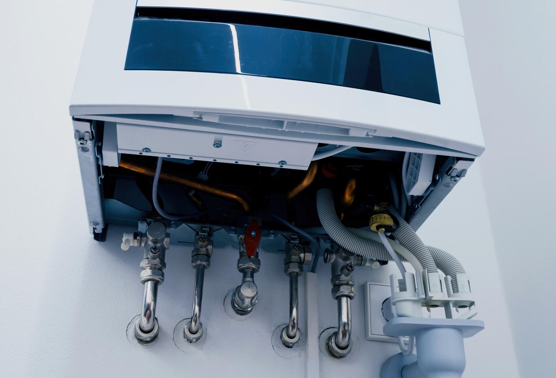 A white wall-mounted boiler with exposed internal components and multiple silver pipes.