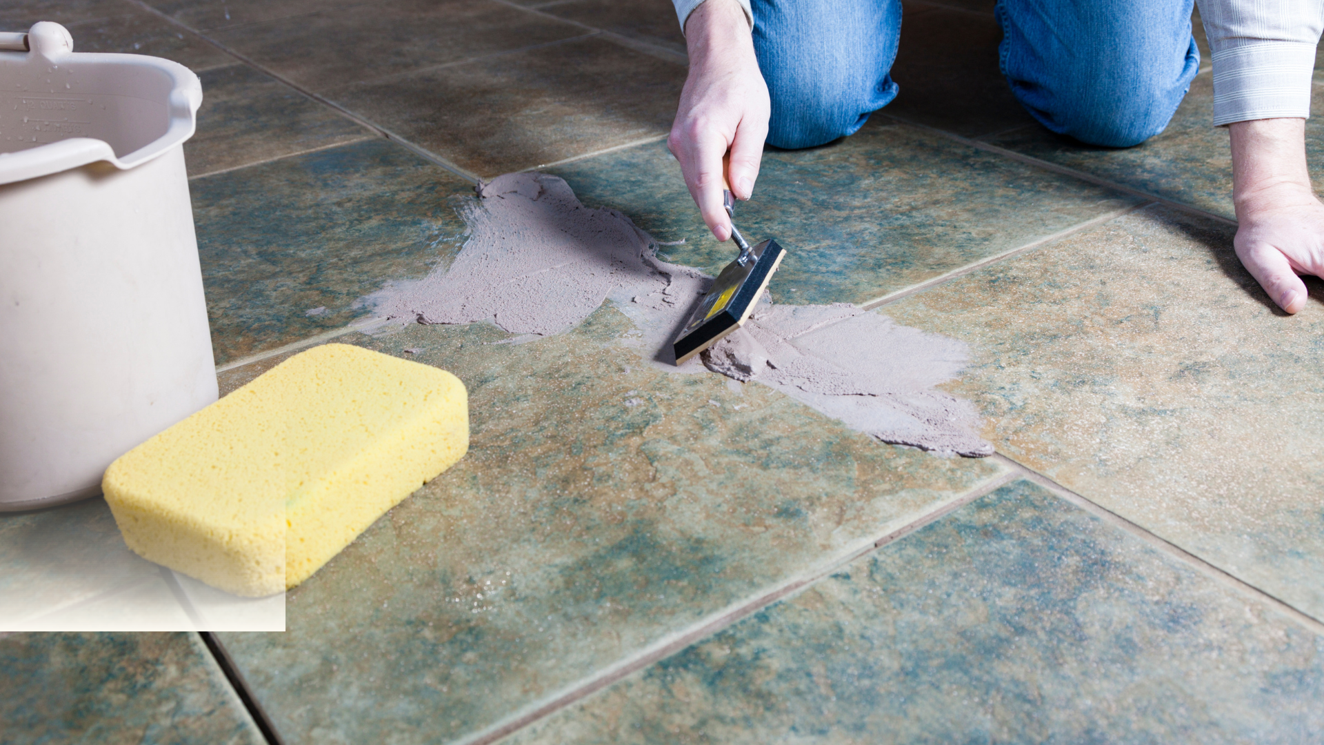 A person is cleaning a tile floor with a spatula and sponge.
