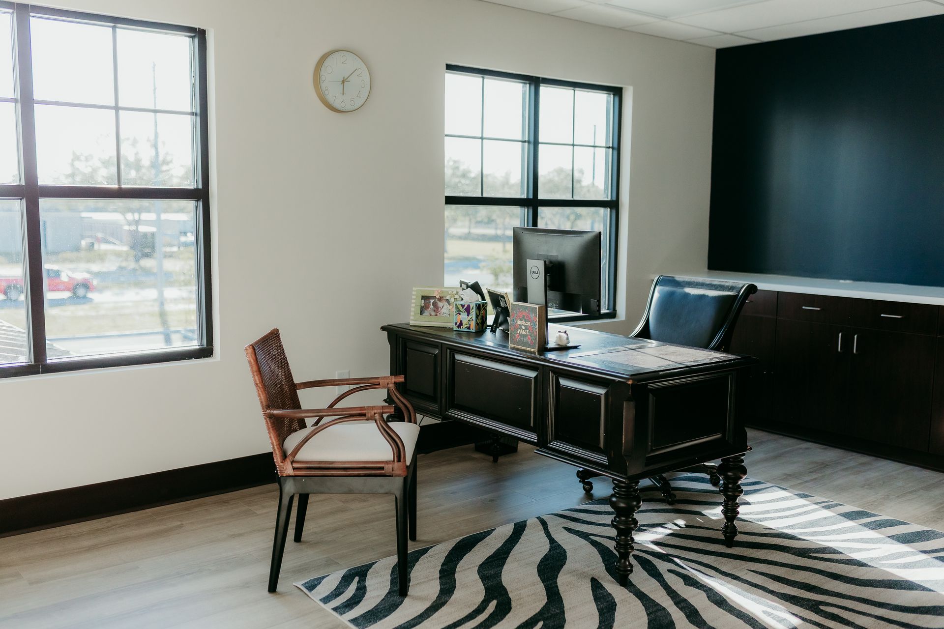 Office with desk, zebra rug, two windows, and dark blue accent wall.