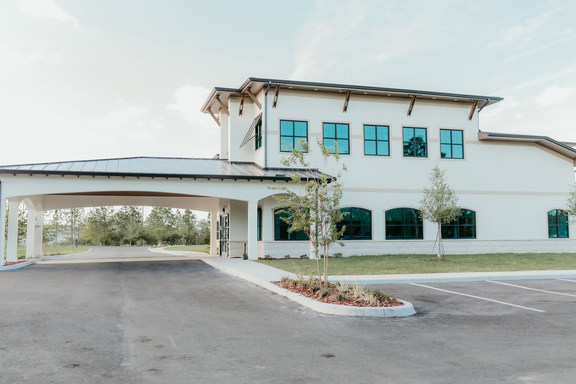 White building with covered drive-through, blue-tinted windows, and a paved parking lot on a sunny day.