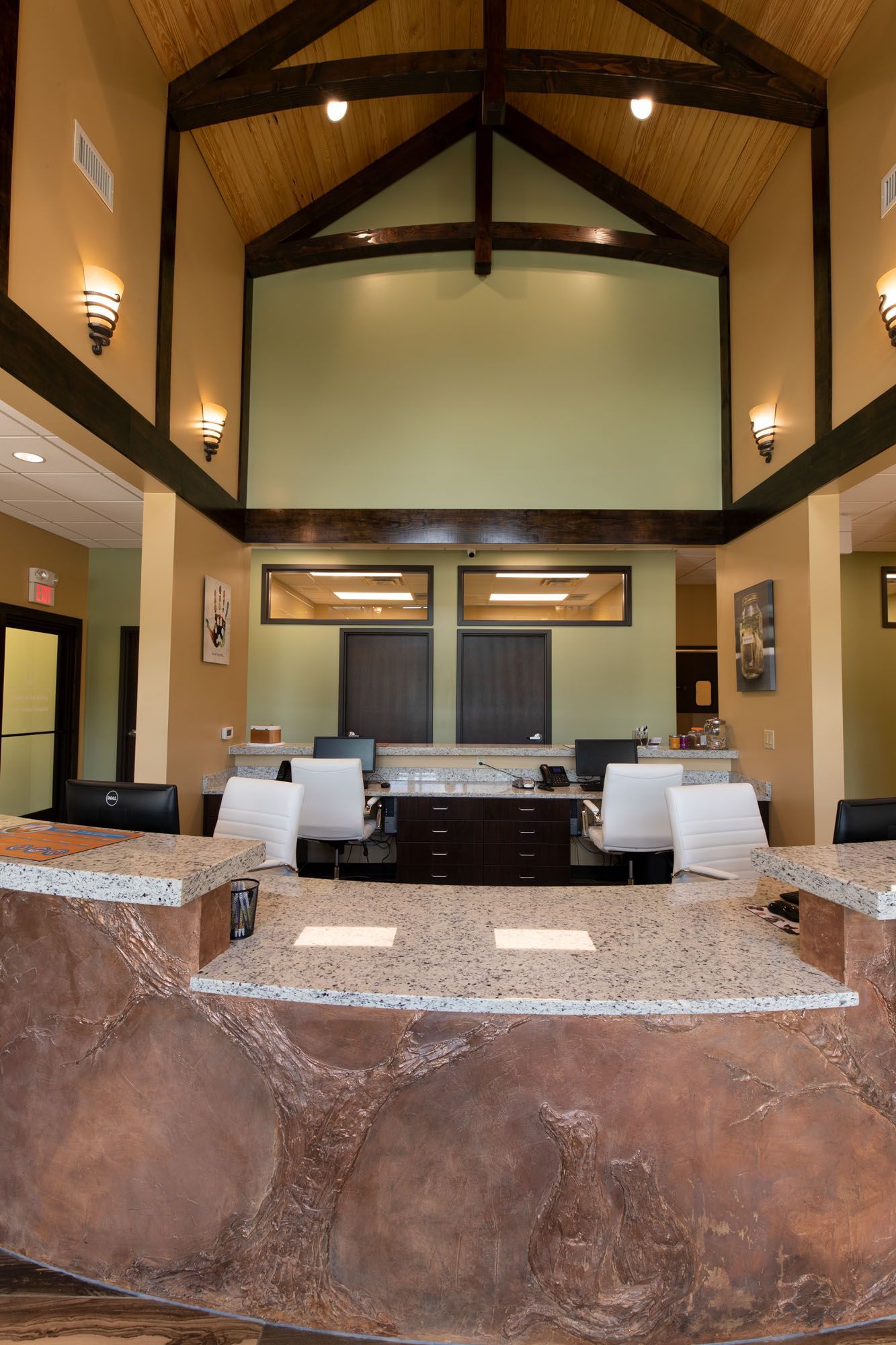 Reception area with stone front desk, high ceilings, wood beams, and green wall.