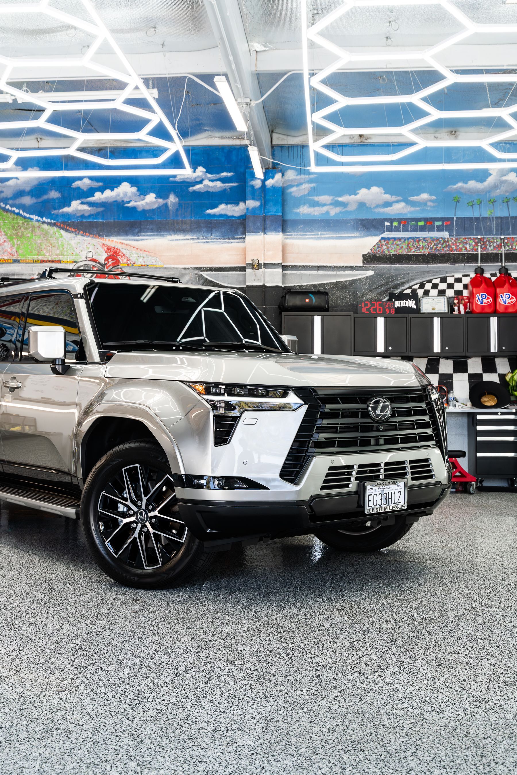 A light-colored SUV with black wheels parked in a bright, modern auto shop with overhead hexagonal lights.