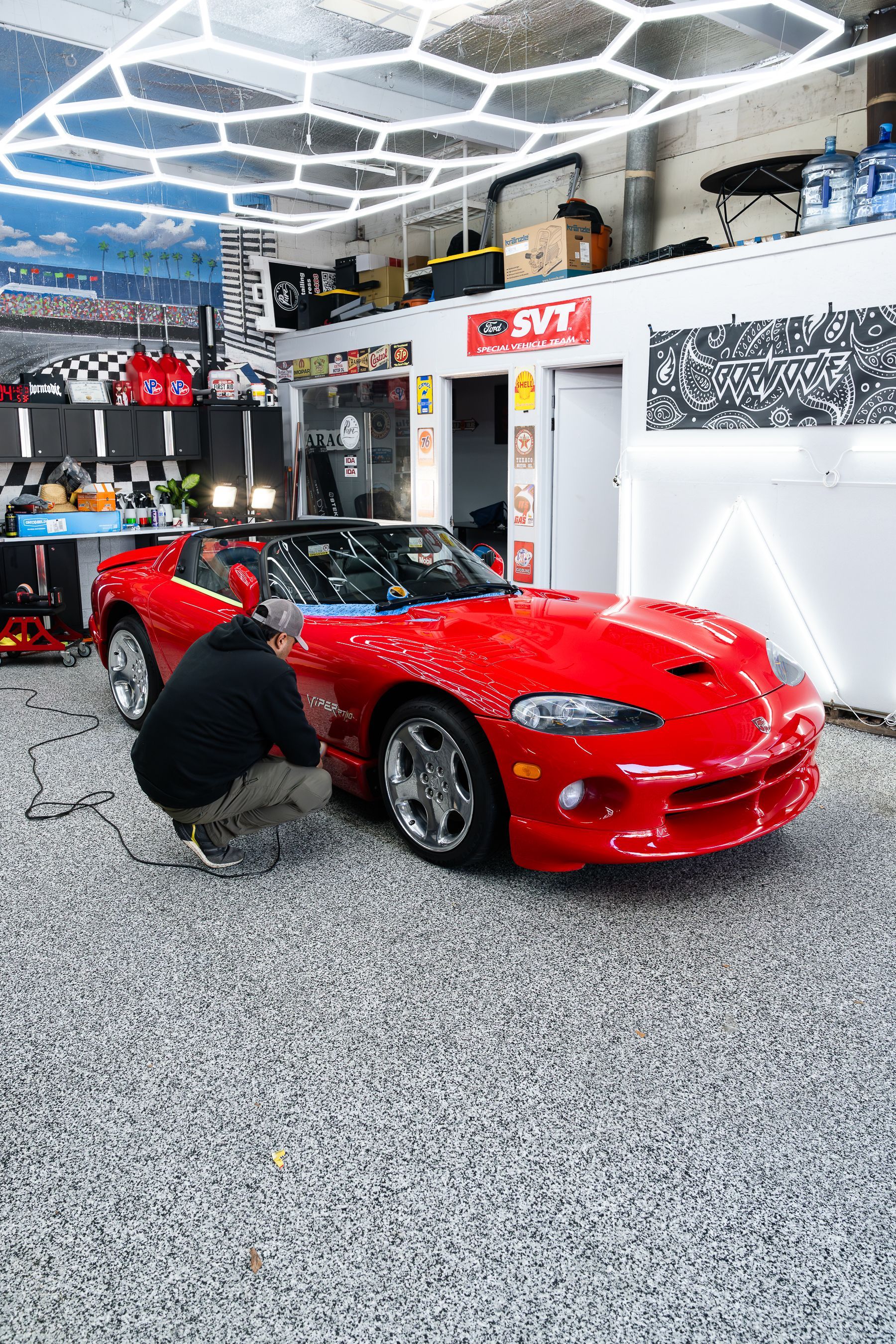 A person kneels to work on the door of a bright red Dodge Viper sports car inside a bright, modern auto garage.
