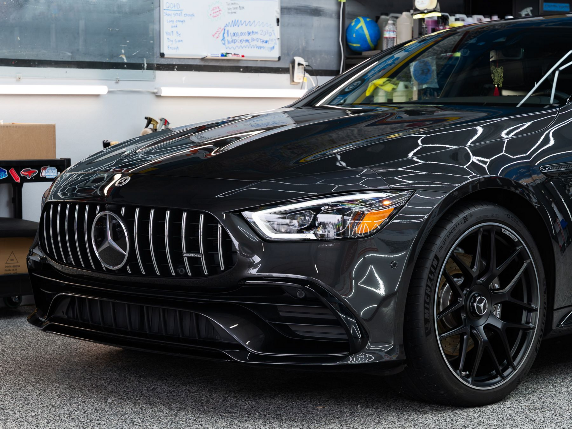 Front-quarter view of a dark grey Mercedes-Benz GT 4-Door Coupe with a Panamericana grille parked in a workshop.