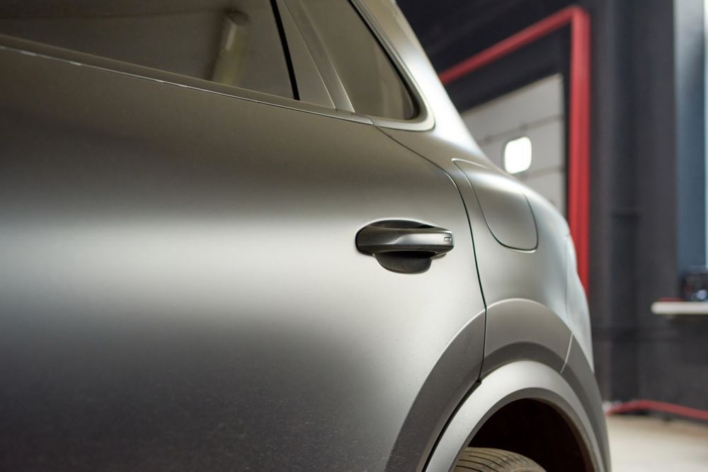 Close-up of a matte-grey car body showing a door handle and rear wheel arch in a garage.