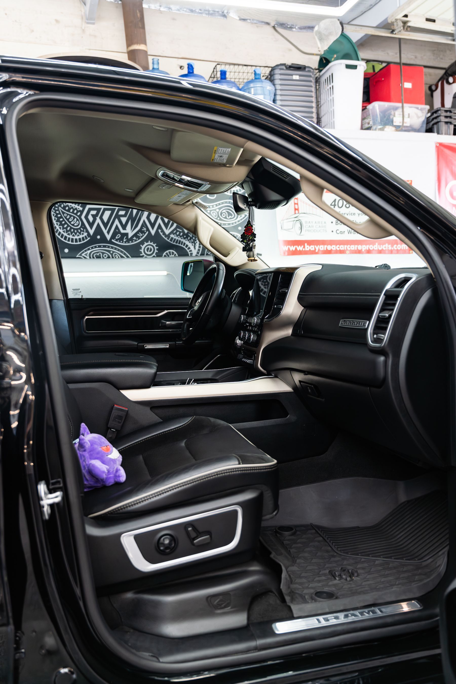 The interior of a black vehicle showing a passenger seat with a purple plush toy and a view of the dashboard.