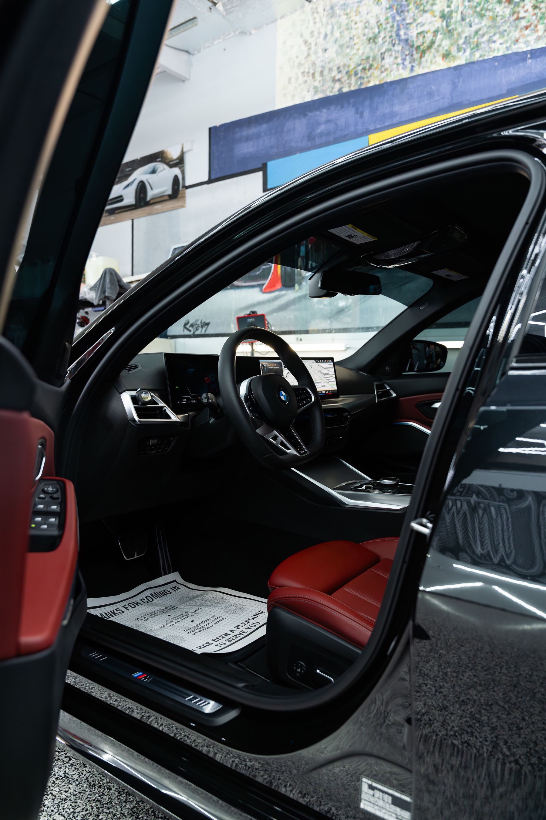 The interior of a black car, featuring red leather seats and a dashboard with a touchscreen, viewed from the open door.