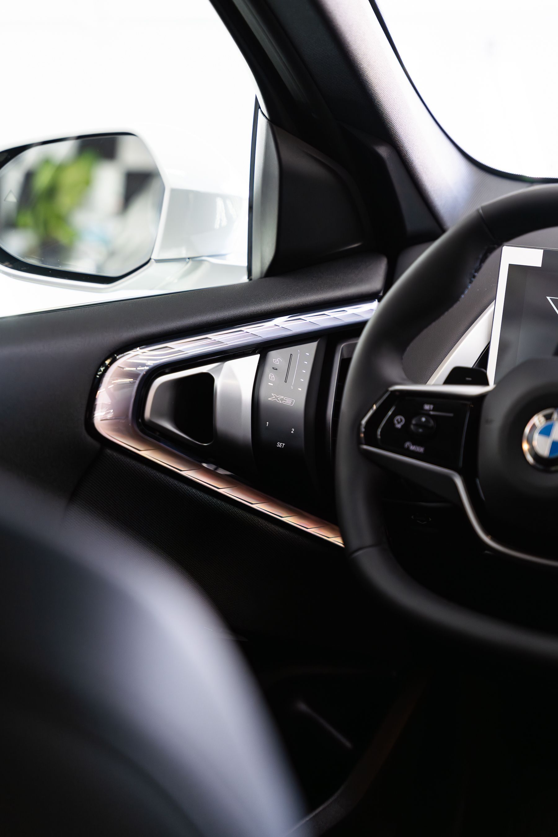 Interior view of a modern BMW vehicle, focusing on the steering wheel, driver-side door panel, and side-view mirror.
