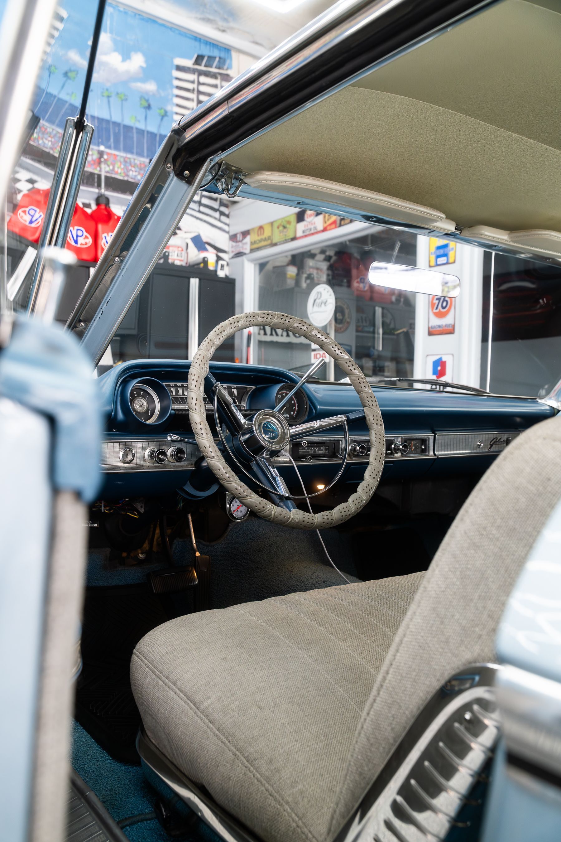 Interior view of a vintage car with a light gray bench seat, textured steering wheel, and blue dashboard.