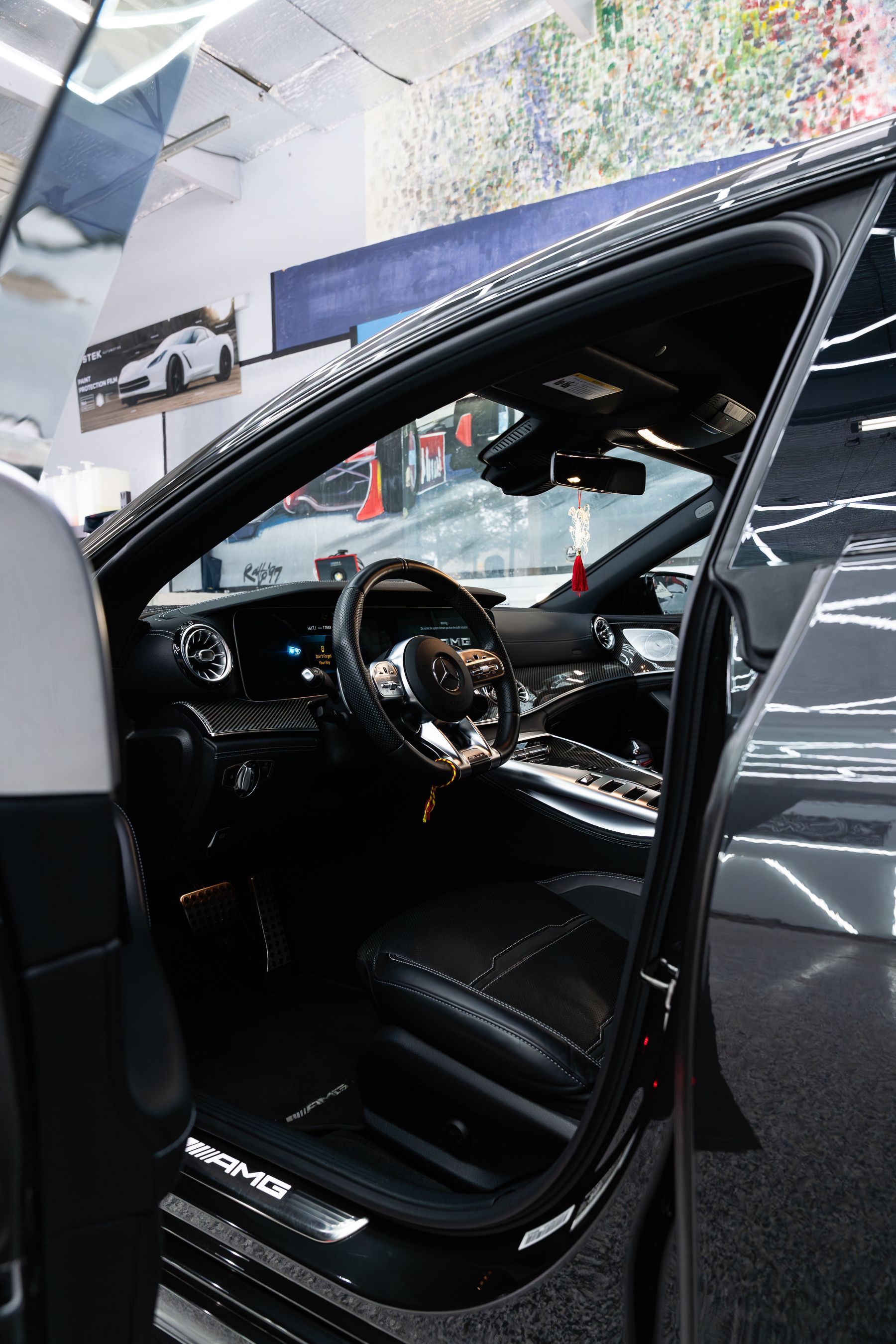 Interior view of a dark luxury car with open door, showing black leather seats and a steering wheel with AMG branding.